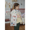 A young girl stands in a child's bedroom wearing a white lace cape decorated with colorful sequins and lip prints, holding a purple toy wand.